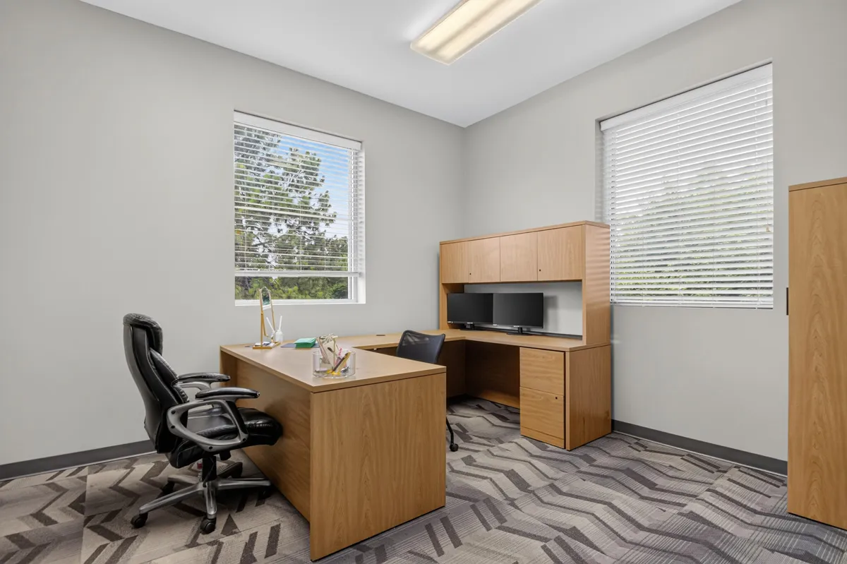 Modern office space with wooden desk, computer, chairs, and natural light